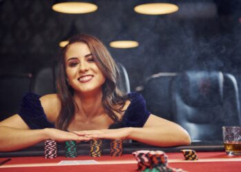 Woman in elegant clothes sits in cassino by table and plays poker game