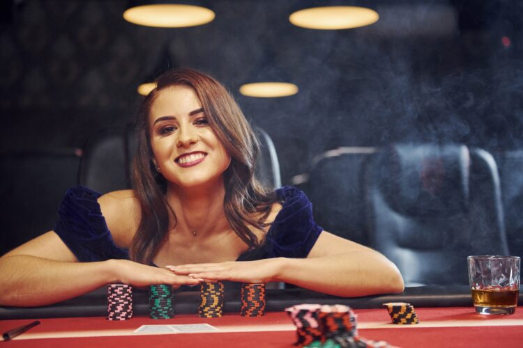 Woman in elegant clothes sits in cassino by table and plays poker game