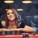 Woman in elegant clothes sits in cassino by table and plays poker game